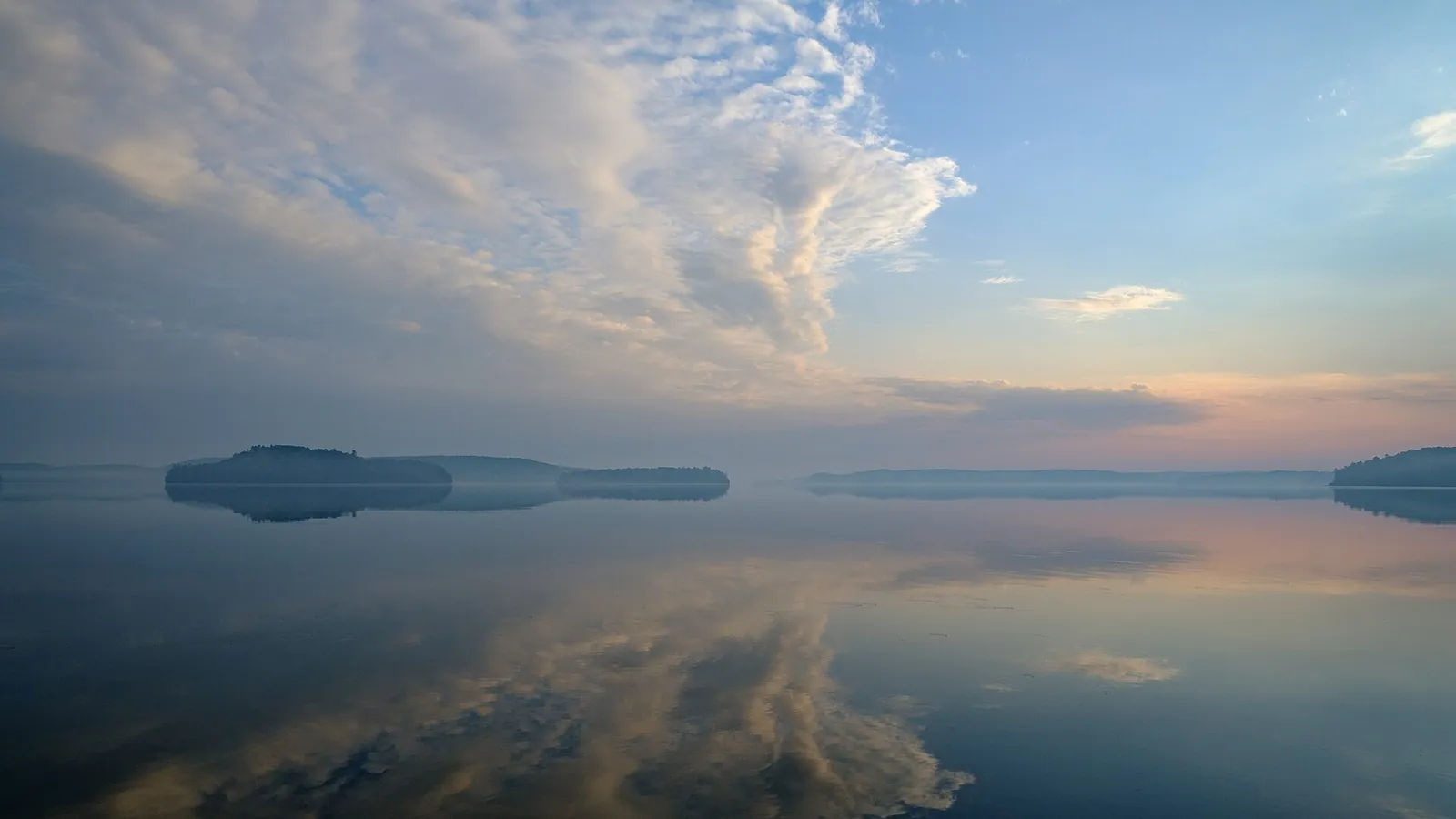 Clouds reflected on calm, misty water at dawn
