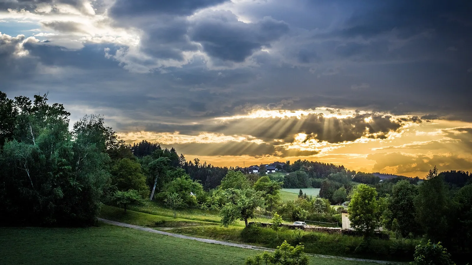 Crepuscular sun rays breaking through dramatic storm clouds over a green valley