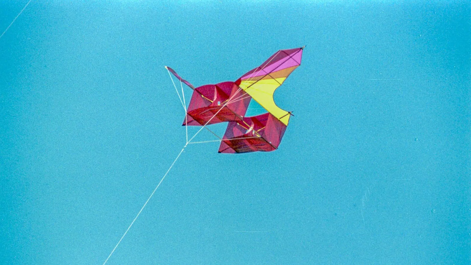 A colourful kite flying on its line against a clear blue sky