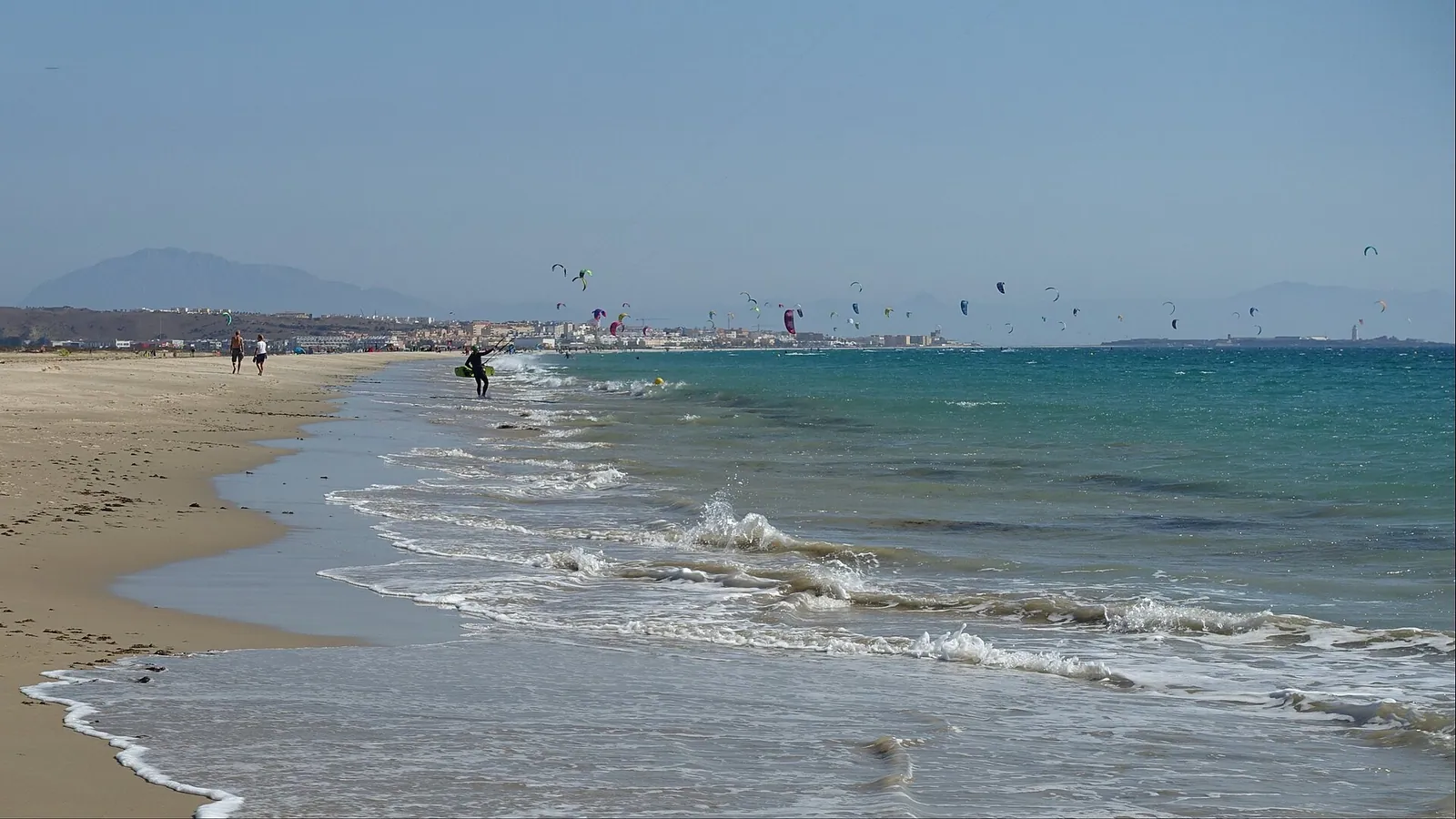 Kitesurfers and colourful kites on the wide sandy beach at Tarifa with the Atlantic behind them