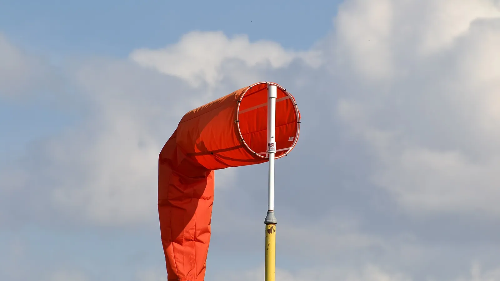 An orange windsock blown straight out in a strong wind against a cloudy sky