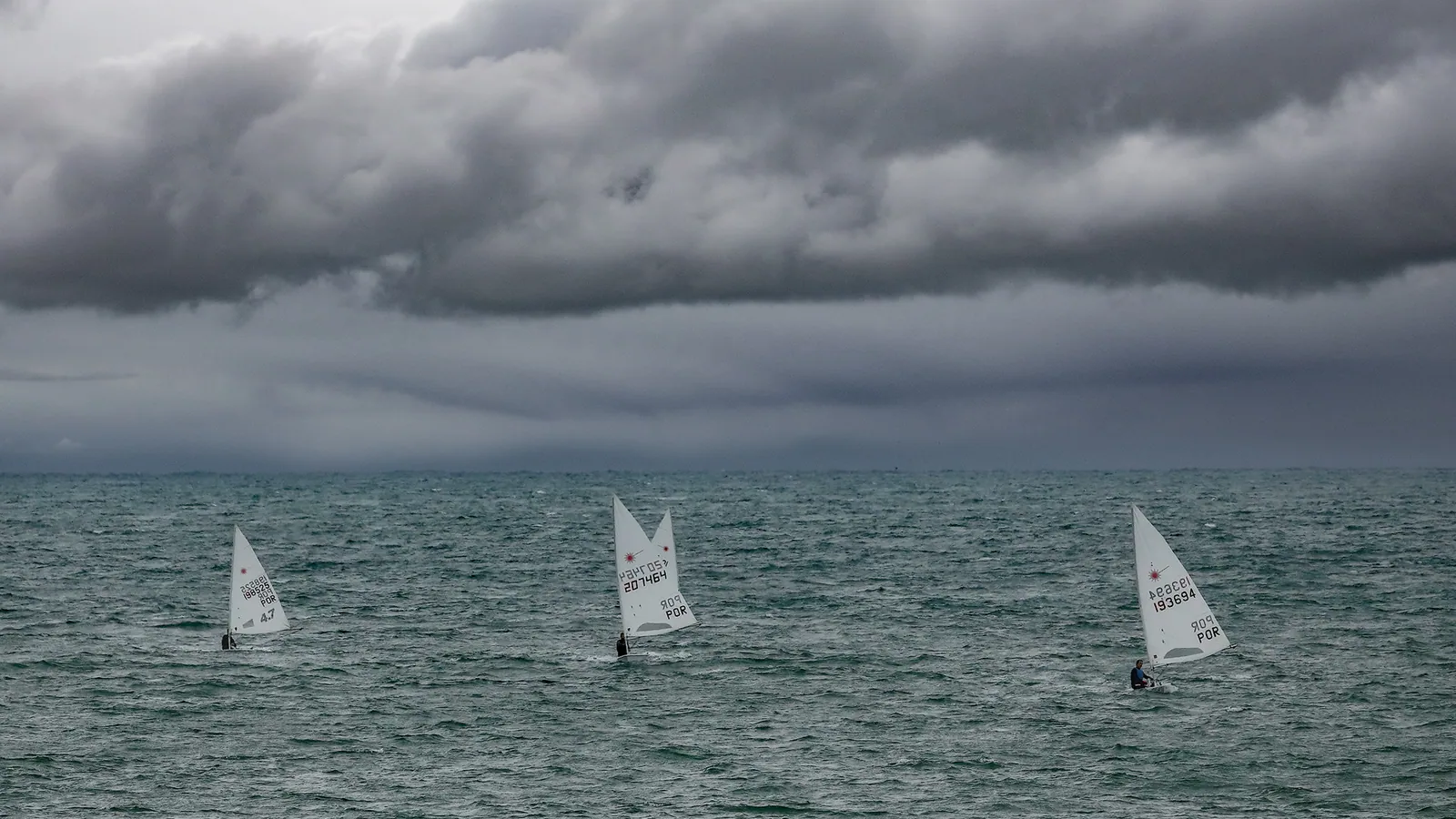 Sailing dinghies on the water under a dramatic, stormy sky