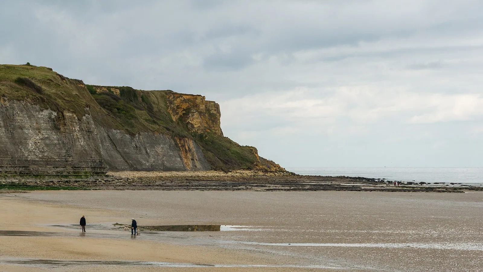 A wide sandy beach at low tide with wind ripples on shallow water