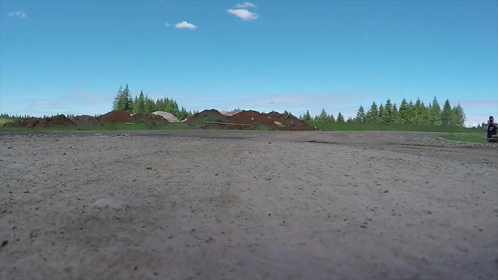 A small camera drone hovering above an open green field under a bright blue sky