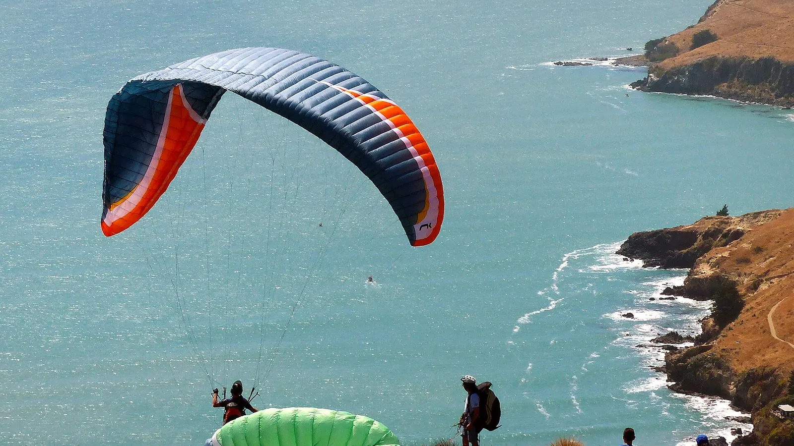 A paraglider pilot launching from a green hillside under a clear sky
