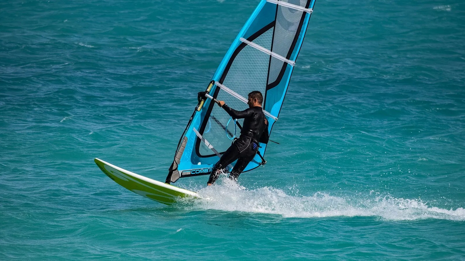A windsurfer planing across choppy blue water with a fully powered sail
